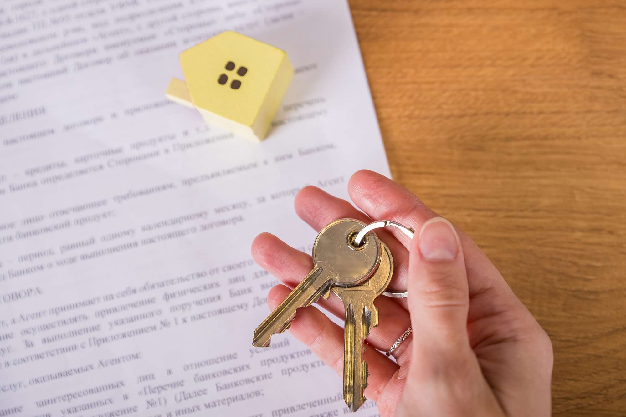 Key is in female hand, documents and small house shaped keychain arrangement on blurred background.